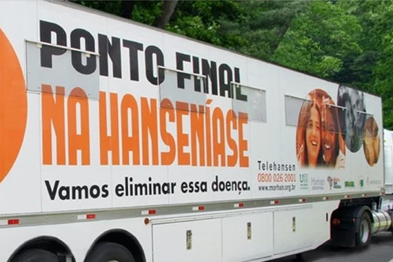 Foto detalhe da carreta branca adesivada com as as frases “Ponto Final na Hanseníase. Vamos eliminar essa doença” escrito em laranja e preto. 